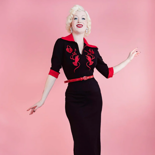 Woman wearing a black dress with red accents against a pink background