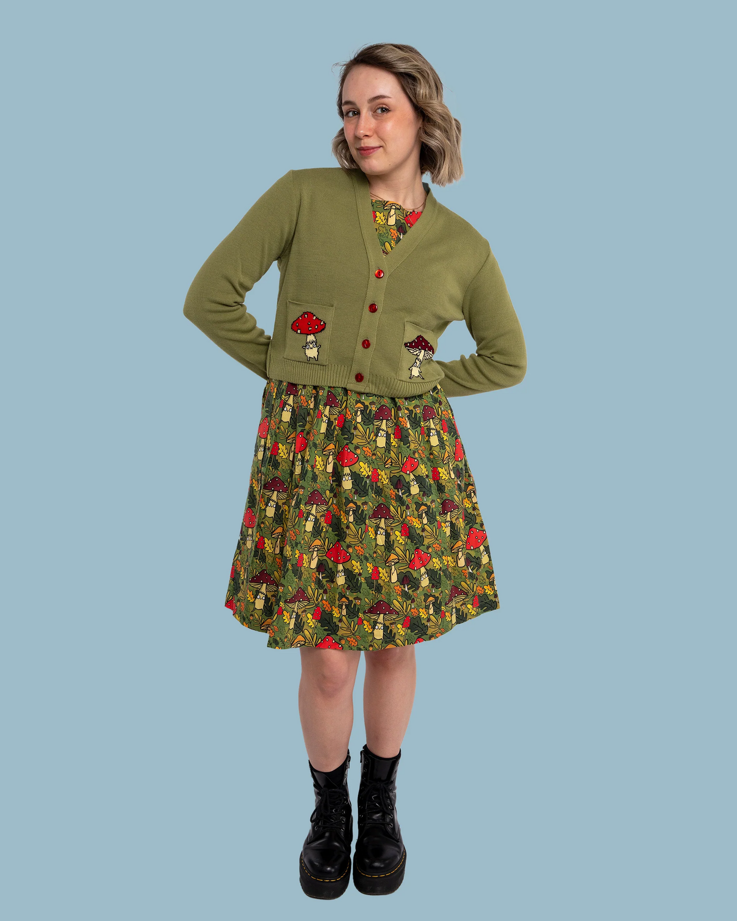 Woman wearing a green cardigan with mushroom patterns and a matching skirt on a blue background