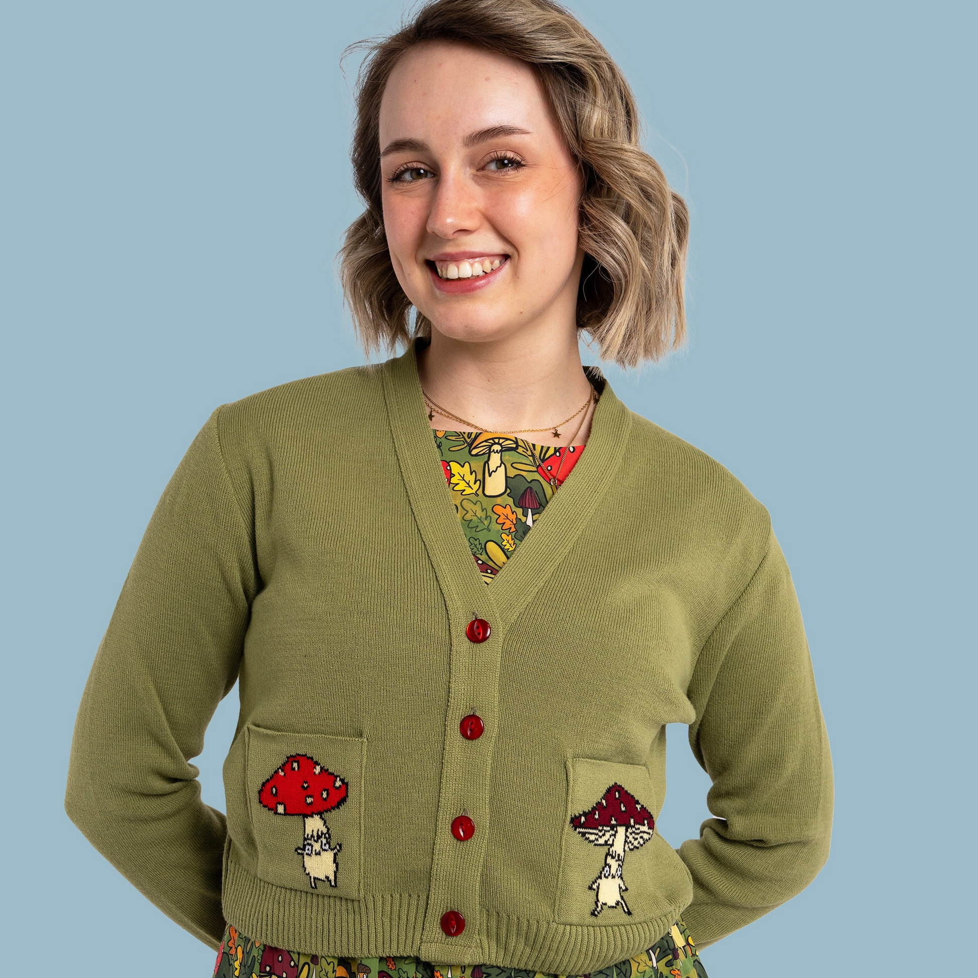 Woman wearing a green cardigan with mushroom designs on a blue background