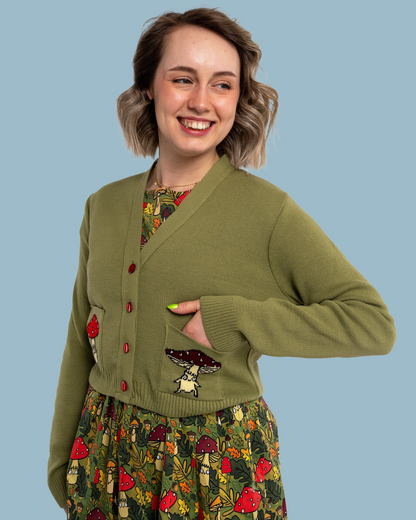 Woman wearing a green cardigan over a floral dress on a blue background