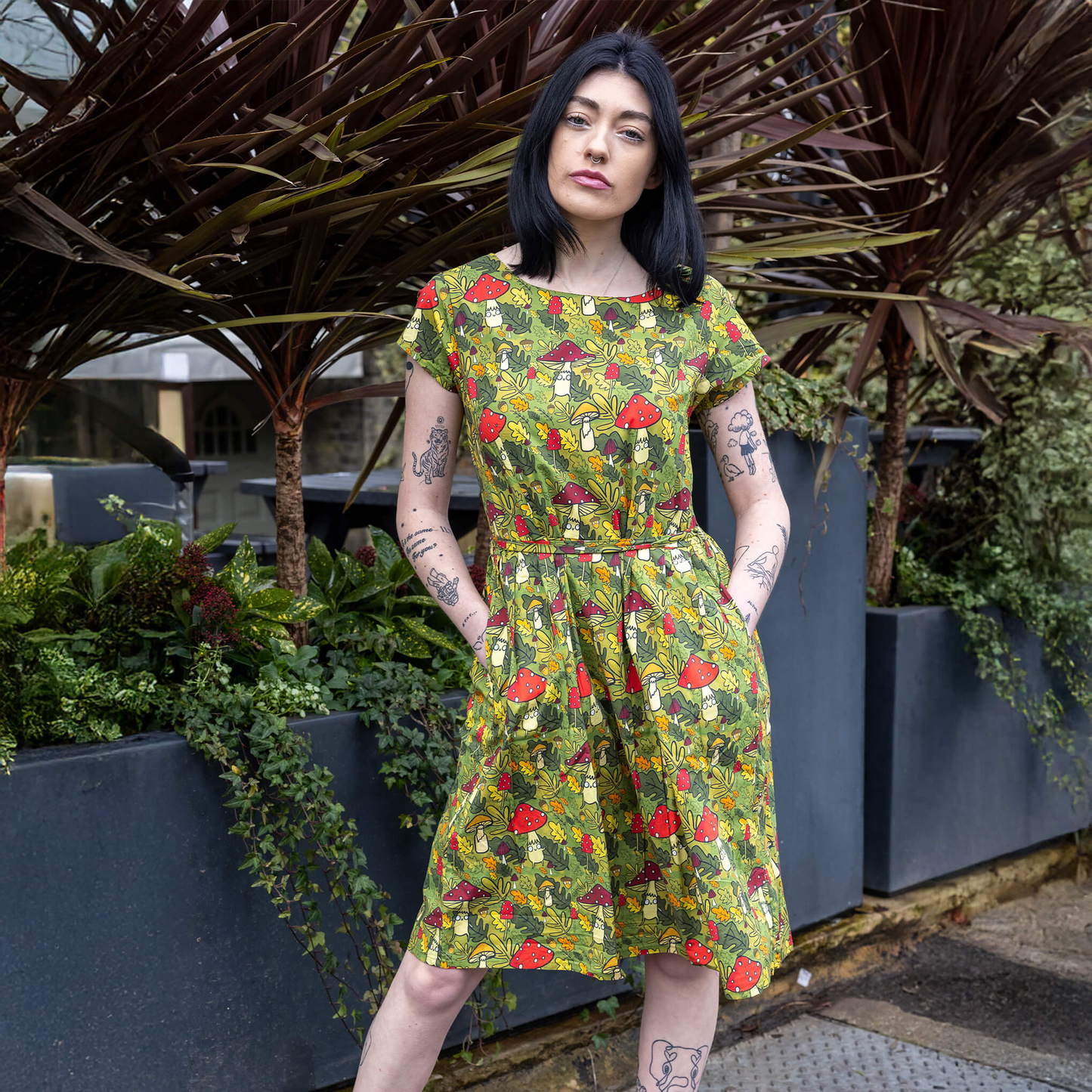 Woman wearing a colorful patterned dress standing outdoors with plants in the background