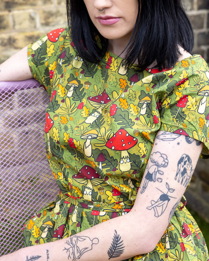Person wearing a green dress with mushroom pattern sitting on a chair.