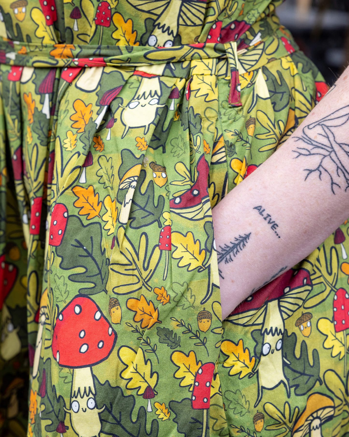 Green robe with nature-themed pattern featuring mushrooms and leaves, worn by a person with tattoos.