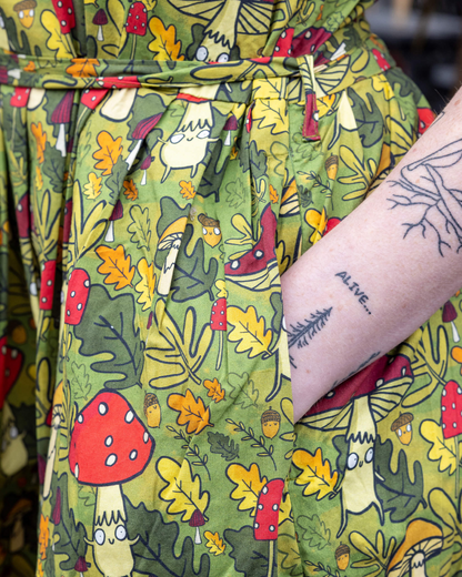 Green robe with nature-themed pattern featuring mushrooms and leaves, worn by a person with tattoos.