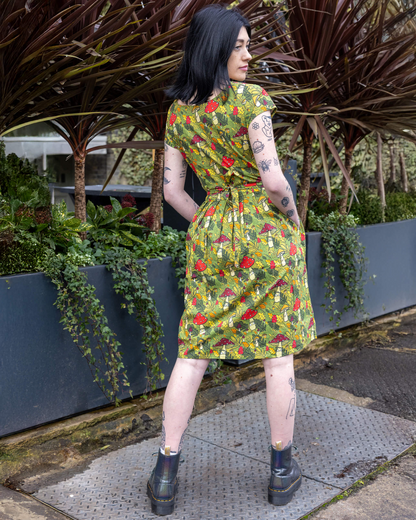 Woman wearing a colorful dress with floral pattern standing outdoors near plants.