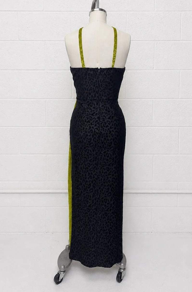 A black leopard-print halter maxi dress displayed on a white mannequin torso against a white brick wall. The dress features lime green shoulder straps and a matching lime green side panel.