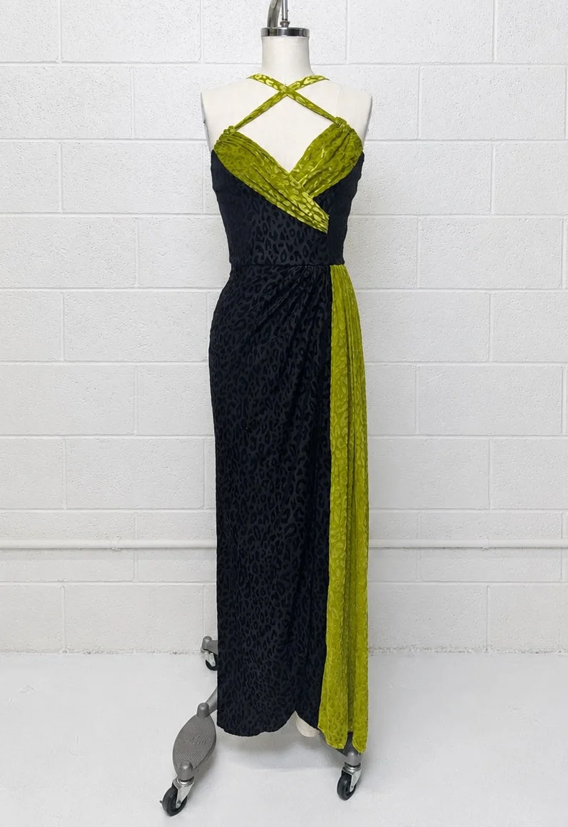 A sleeveless halter maxi dress displayed on a mannequin against a white brick wall. The dress features a black leopard-print body with lime green textured trim along the halter straps, sweetheart neckline, and side drape.