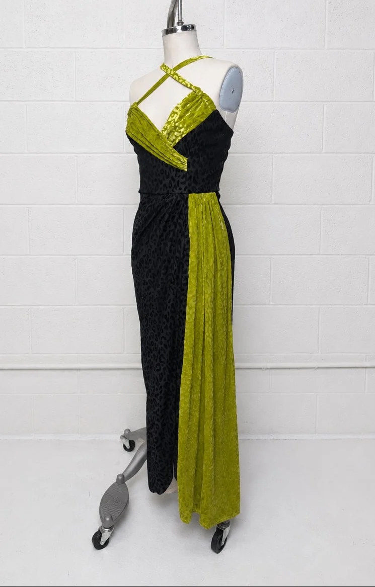 A sleeveless halter-neck maxi dress displayed on a mannequin against a white brick wall. The dress features a textured black body with a draped lime green overlay at the bust and a matching lime green side panel.