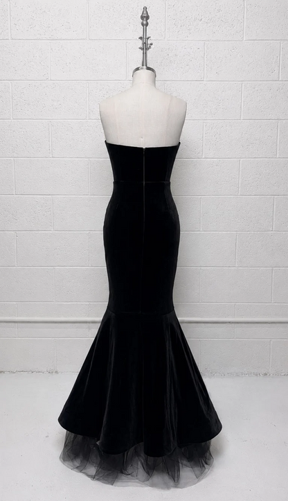 A strapless black mermaid gown displayed on a white mannequin torso against a white painted brick wall.