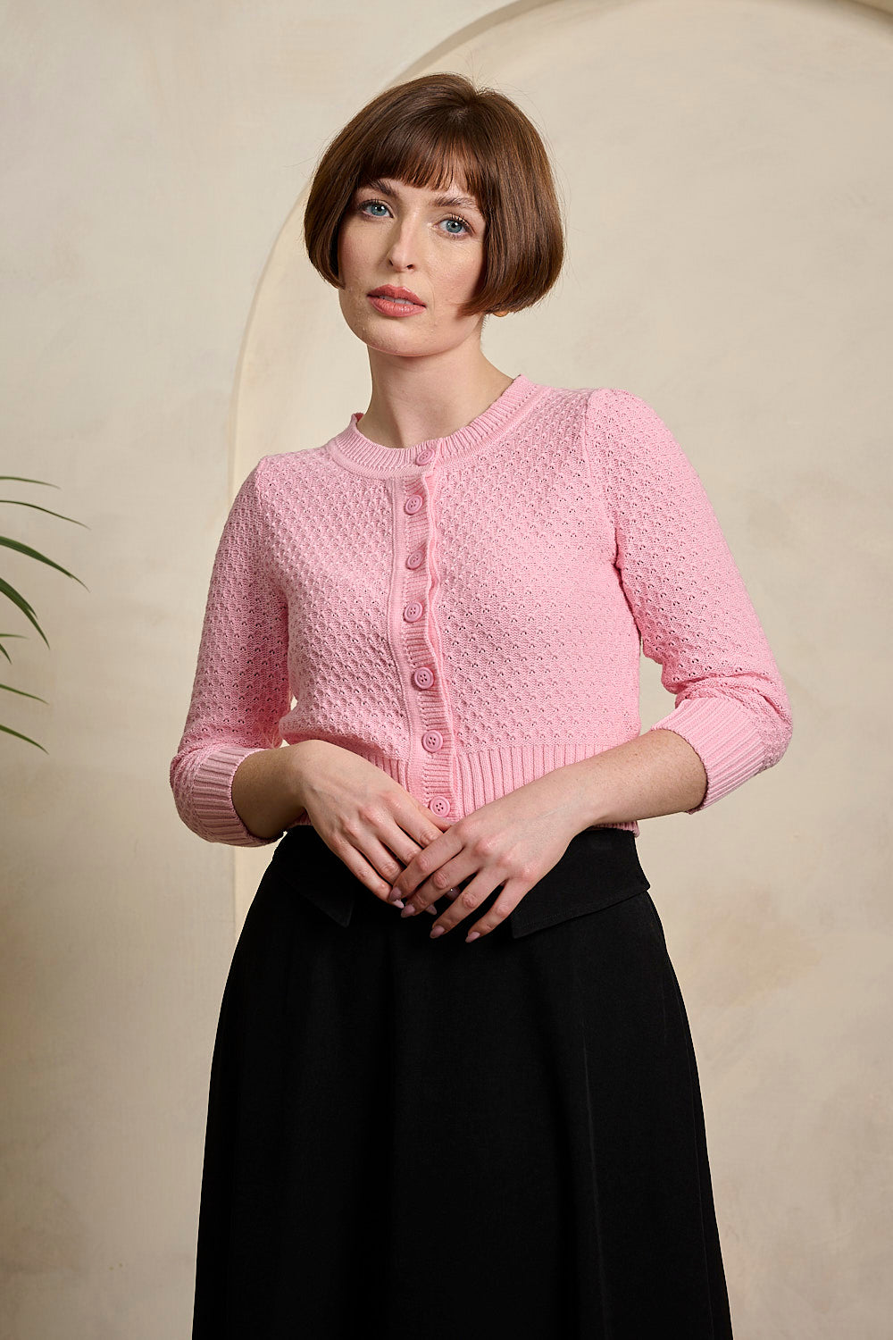 Woman wearing a pink knitted cardigan against a beige background