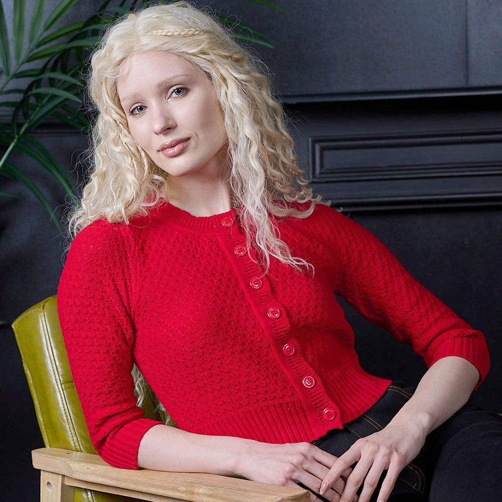 Woman wearing a red sweater sitting on a green chair against a dark wall.
