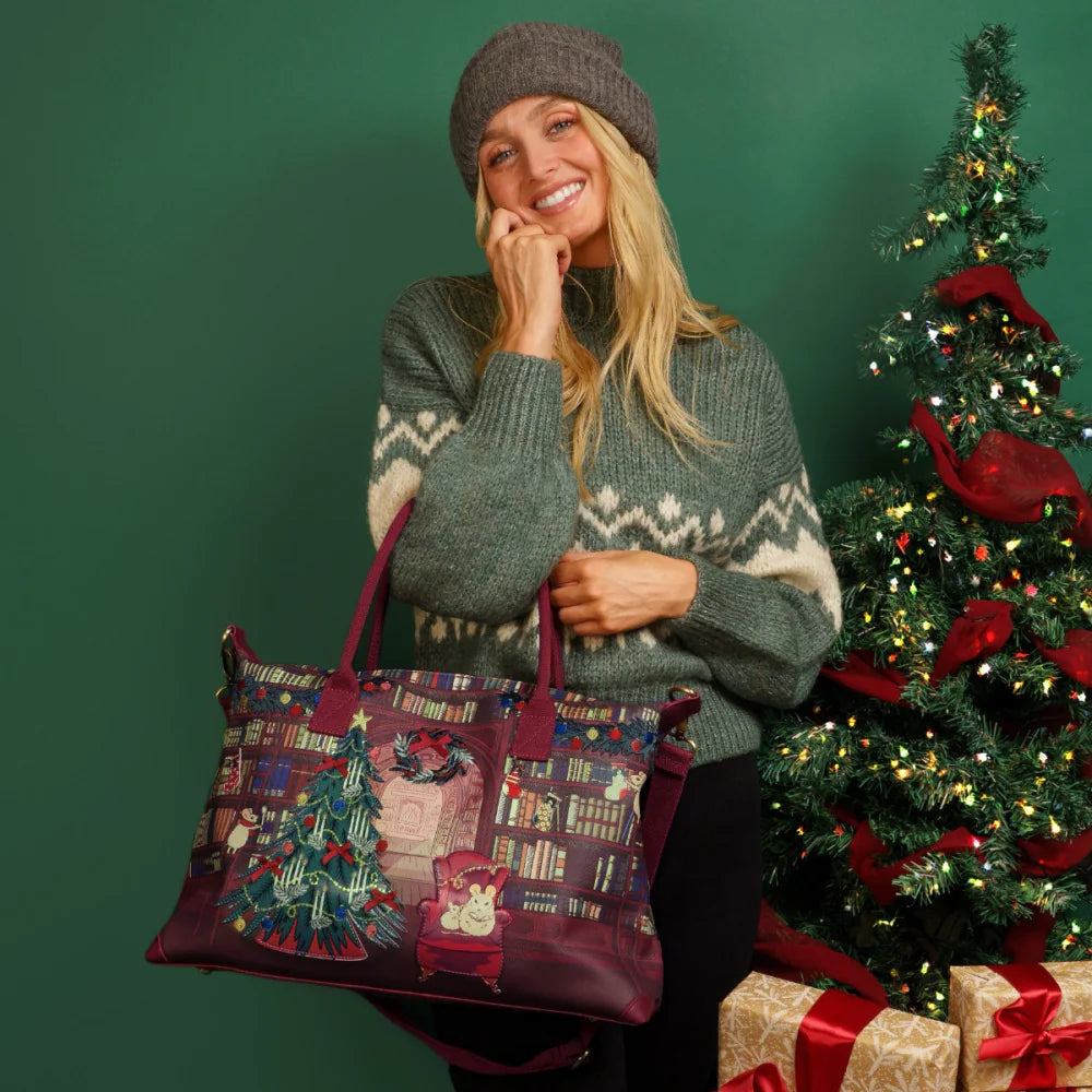 Woman holding a Christmas-themed bag in front of a decorated tree and presents.