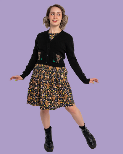 Person wearing a black cardigan with cow pockets and a floral skirt on a purple background