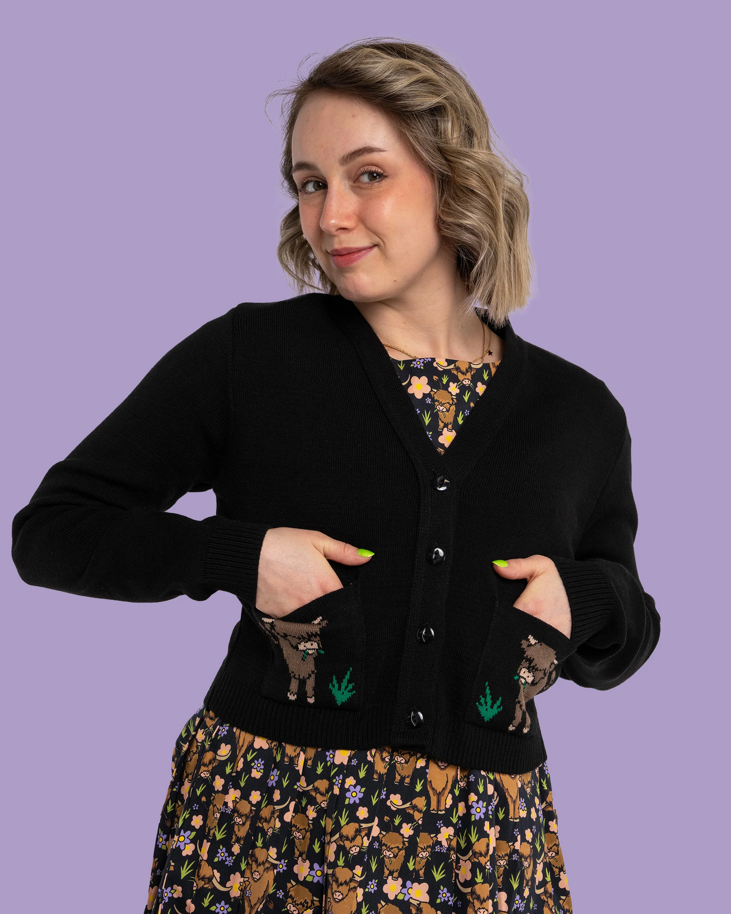 Woman wearing a black cardigan cow with embroidered designs on a purple background